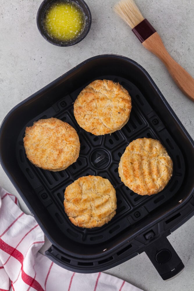 Four biscuits in an air fryer basket. They're flipped for the second half of baking and there are indentations in the bottom from the shape of hte air fryer basket. 
