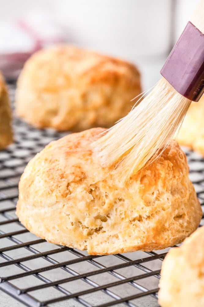 A close up of a biscuit getting butter brushed on top.