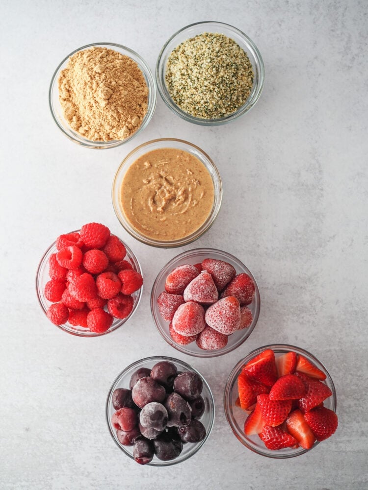 Ingredients for mixing into a chocolate protein shake for various flavor combinations including: fresh raspberries, fresh strawberries, peanut butter powder, fresh ground peanut butter, frozen strawberries, frozen cherries, and hemp seed.