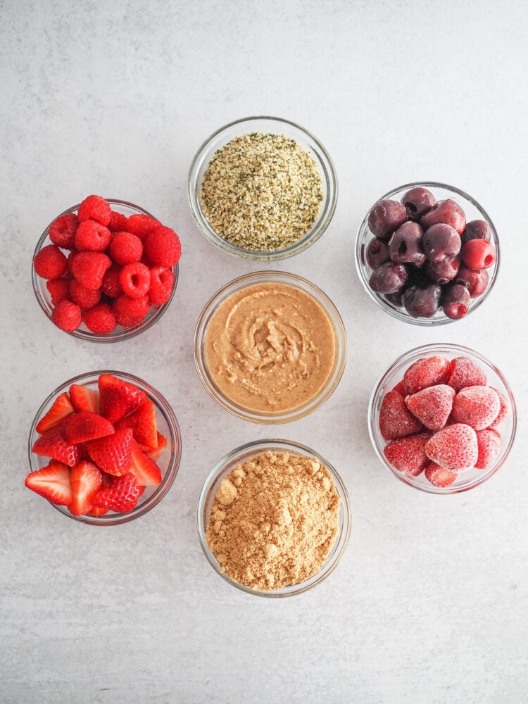 Ingredients for mixing into a chocolate protein shake for various flavor combinations including: fresh raspberries, fresh strawberries, peanut butter powder, fresh ground peanut butter, frozen strawberries, frozen cherries, and hemp seed.