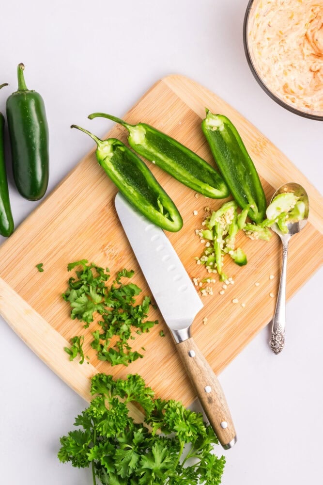 chopped parsley and sliced jalapenos on a cutting board with a knife and spoon.