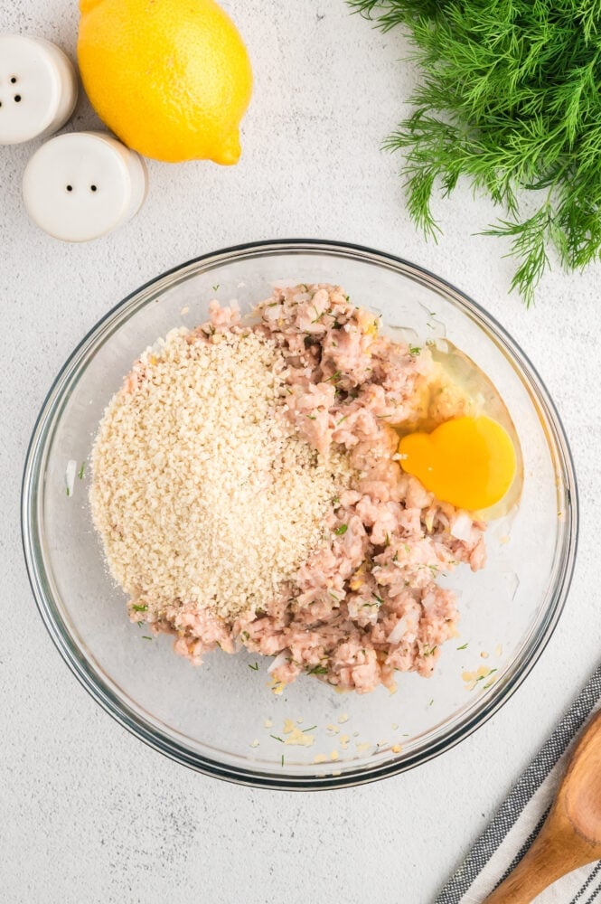 Ground chicken in the process of being mixed into meat balls with a raw egg and panko bread crumbs added on top.