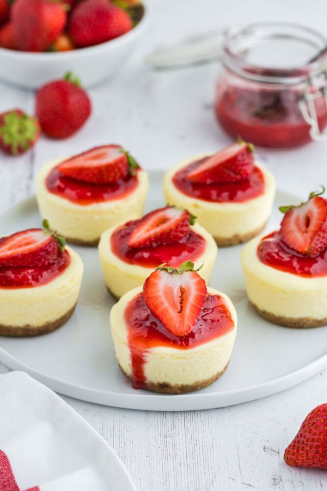 Cheesecake bites topped with strawberries on a white serving plate