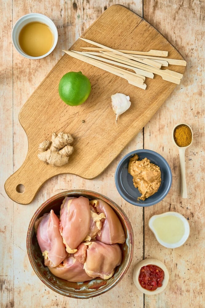 bowl of raw chicken thighs surrounded by ingredients to make thai chicken satay marinade