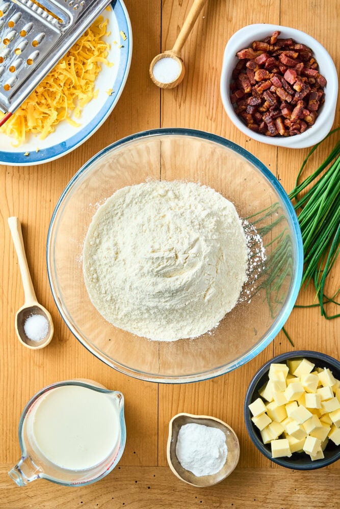 ingredients for making bacon cheddar scones measured out into bowls and on a wood table