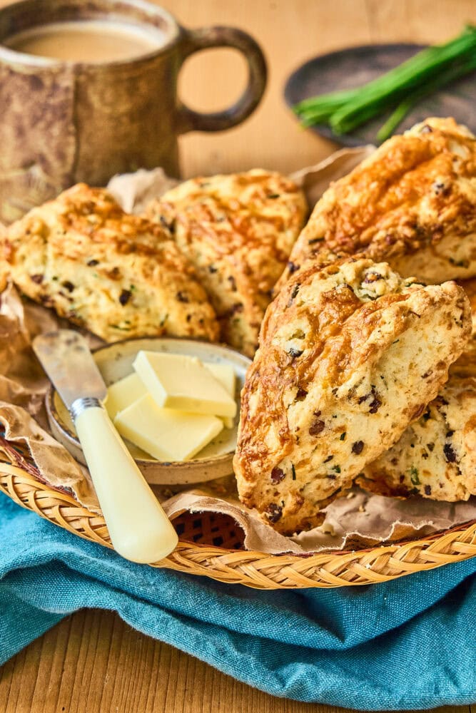 bacon cheddar scones on a wicker basket plate with a butter and a butter knife and coffee in the background