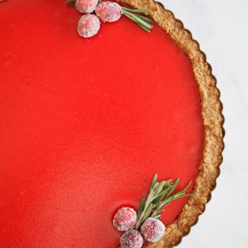 Overhead photo of a bright burgundy cranberry tart garnished with sugared cranberries and rosemary.