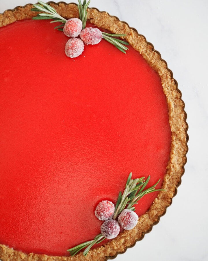 Overhead photo of a bright burgundy cranberry tart garnished with sugared cranberries and rosemary.