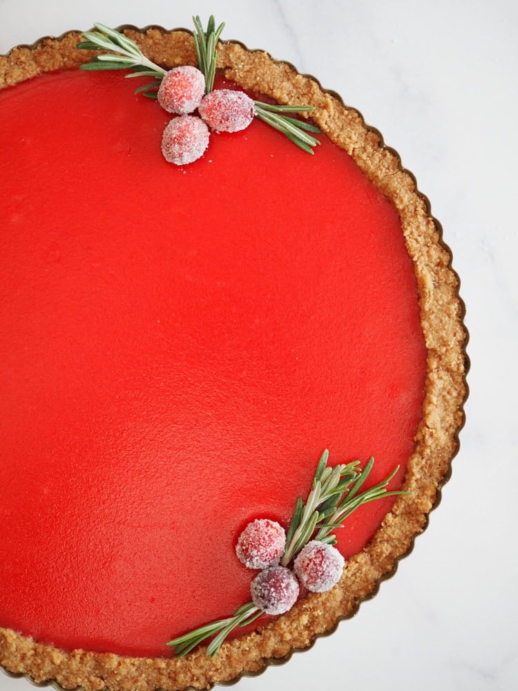 Overhead photo of a bright burgundy cranberry tart garnished with sugared cranberries and rosemary.