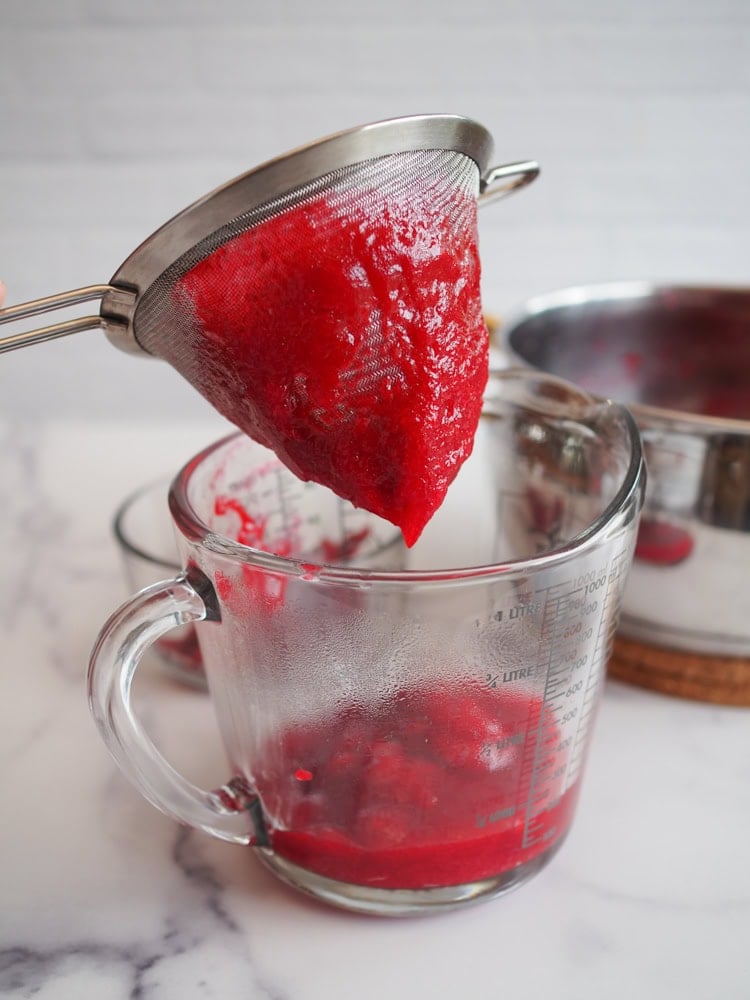 Cranberry sauce getting pressed through sieve into glass container