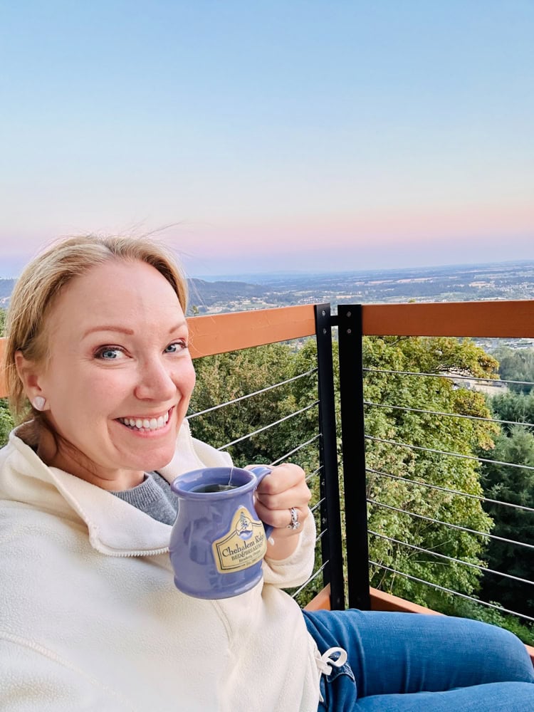 Rachelle holding lavender mug and smiling while on the balcony at her bed and breakfast