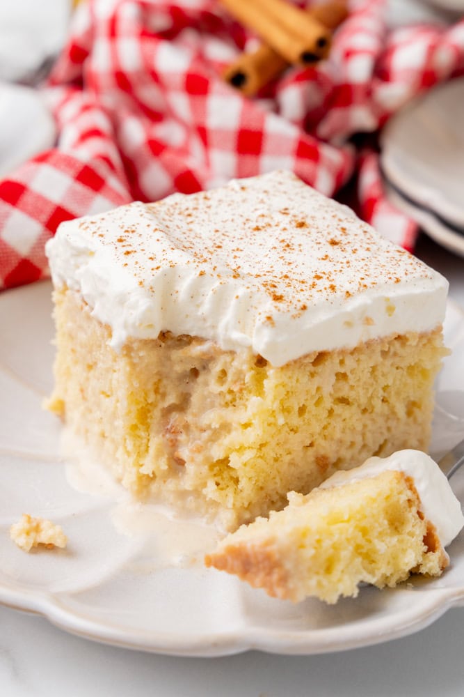 Coquito tres leches cake with a bite on a fork and a red and white checkered towel in the background