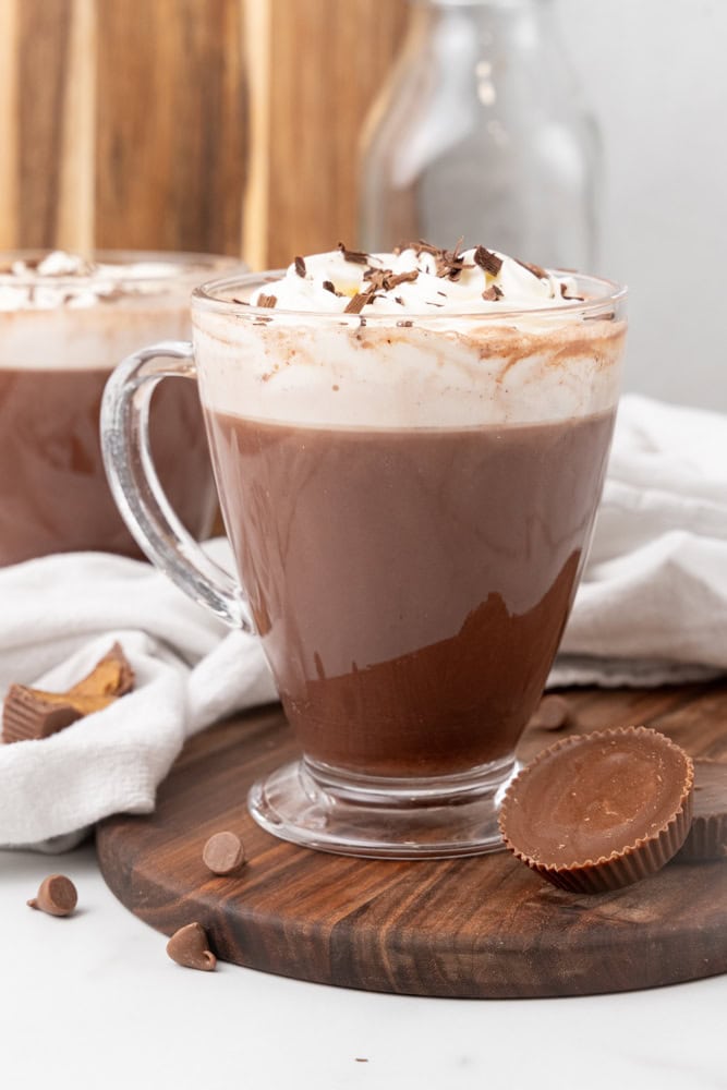 clear mug of peanut butter hot chocolate topped with whipped cream and chocolate shavings