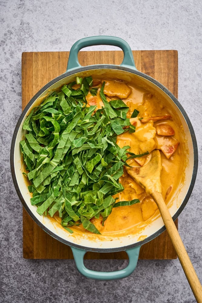 adding greens to cook in Thai pumpkin curry