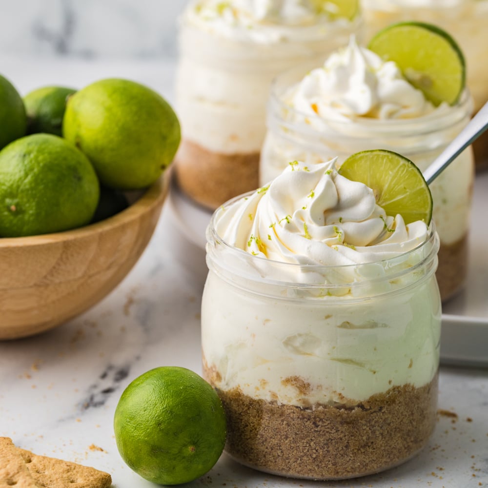 Jar of no bake key lime cheesecake in a clear glass jar garnished with key lime, and a whole key lime to the side