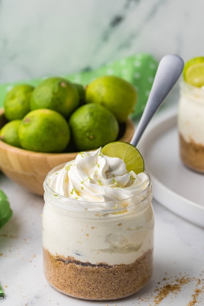 no bake key lime cheesecake in a jar with a bowl of key limes behind it