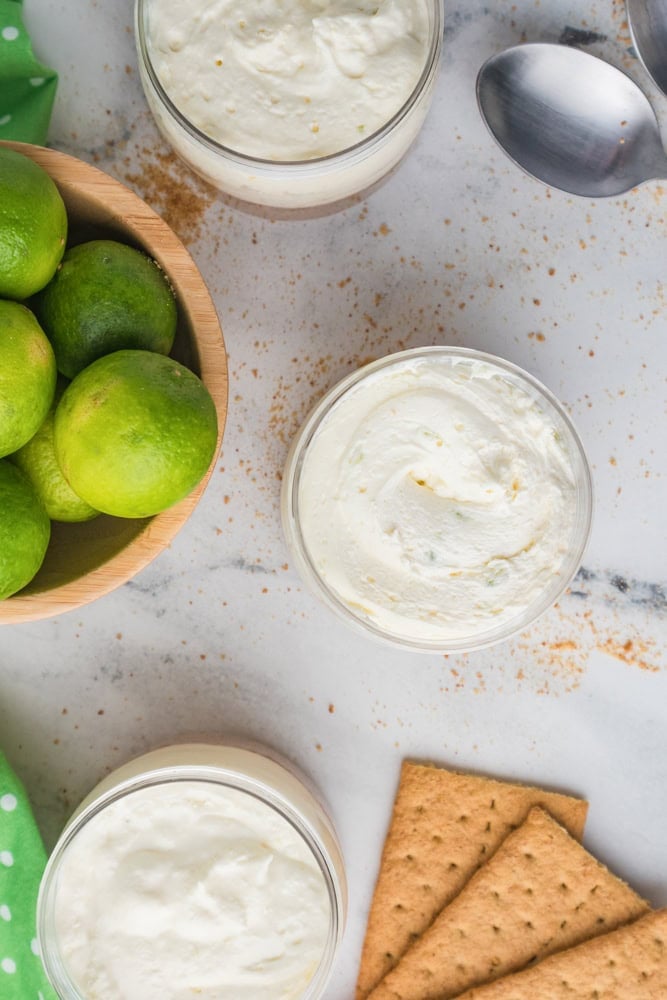 Overhead view of no bake key like cheesecakes in a jar with a bowl of key limes