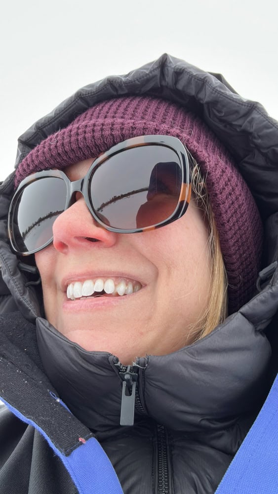 Rachelle showing layers of beanie hat, down puffer jacket, and tour-provided snow suit.