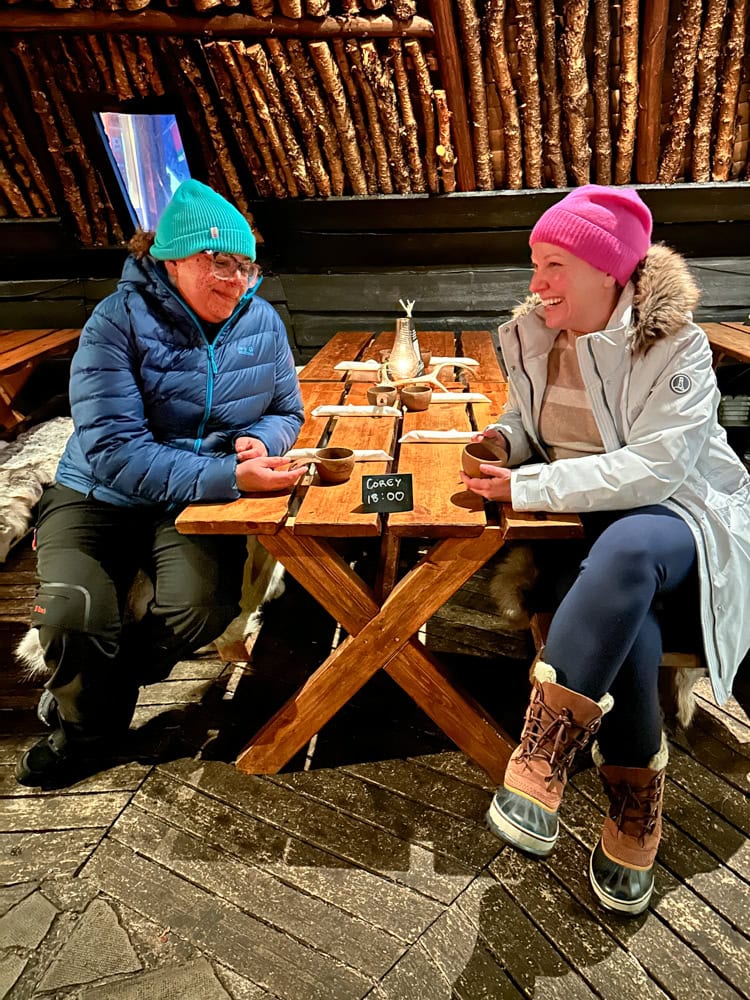Rachelle at dinner with a friend wearing fleece lined leggings, parka, Sorel boots, and a pink beanie hat.