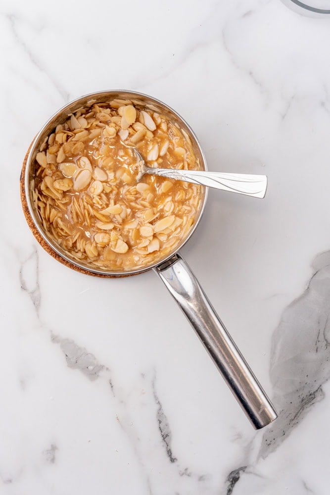 caramelized slivered almonds in a stainless steel pan with a spoon