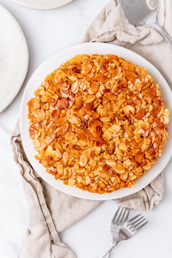 overhead look at a finished almond tart on a white serving plate. The almonds look caramelized and crispy