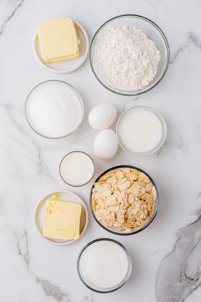 ingredients for making almond tart pre-measured in clear glass bowls on a marble countertop