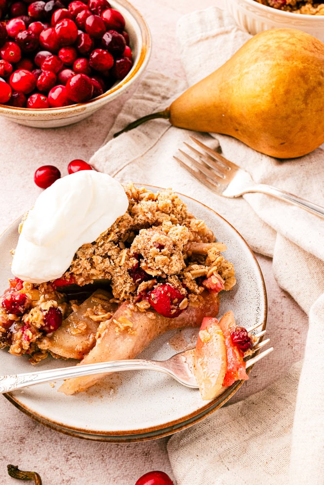 serving of pear crisp with cranberries on a plate with a dollop of whipped cream