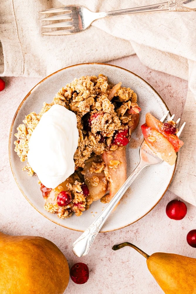 overhead view of pear crisp on a plate with a fork and a dollop of whipped cream
