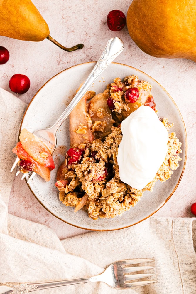 overhead view of a serving of pear crisp with a dollop of whipped cream and a fork