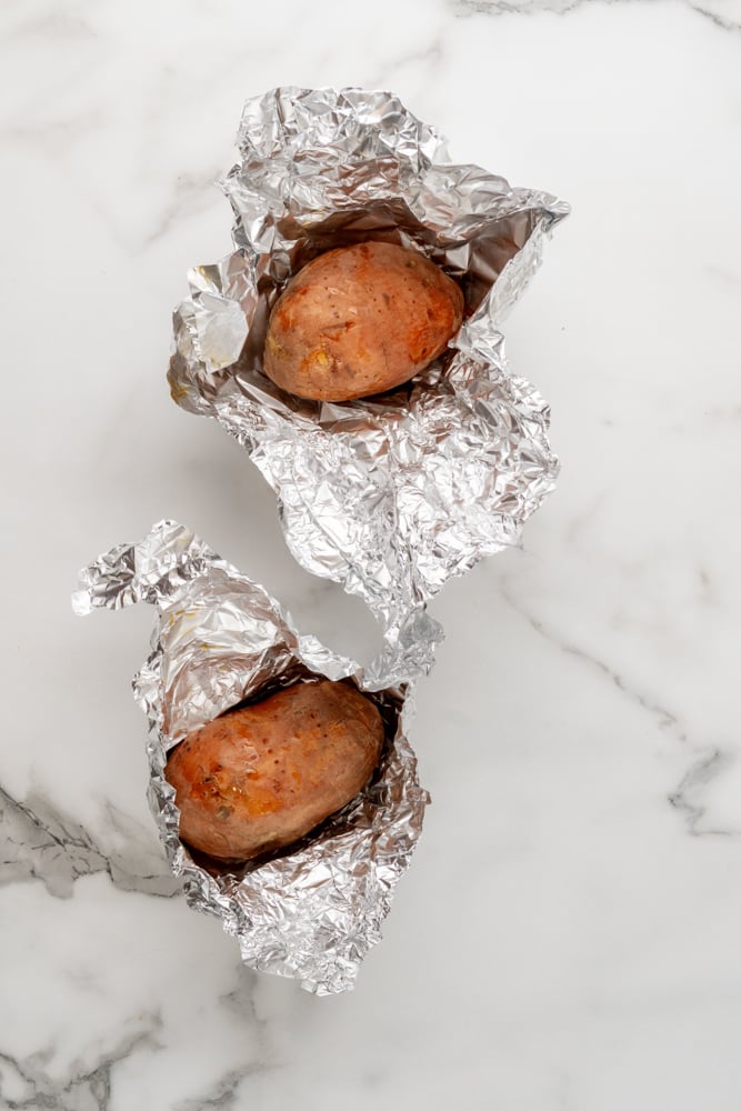 two sweet potatoes wrapped in foil fresh out of the oven