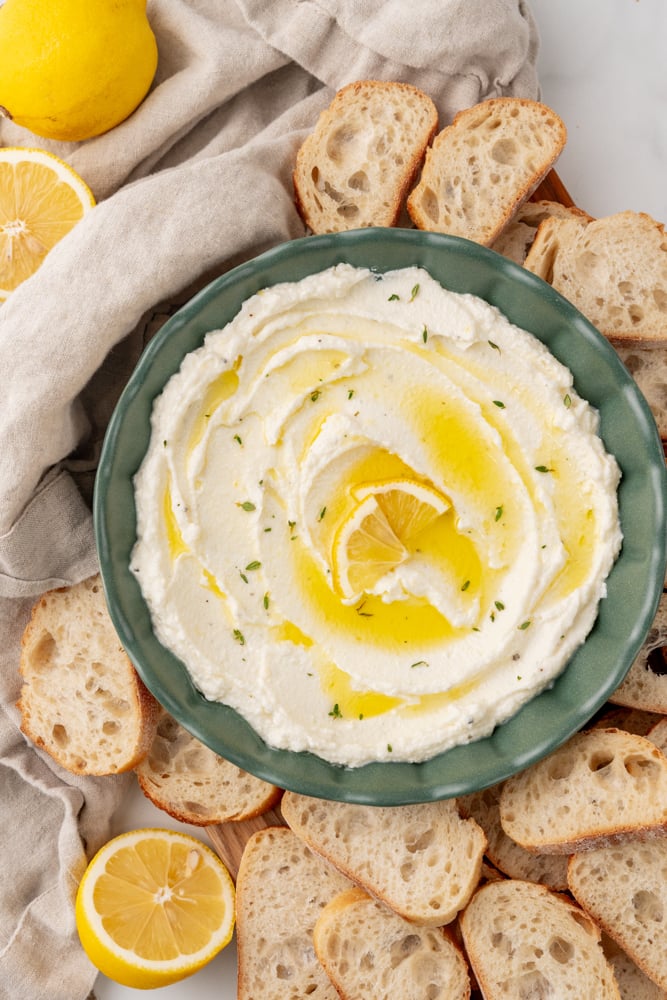 Overhead look at a bowl of whipped ricotta dip surrounded by little toasts.