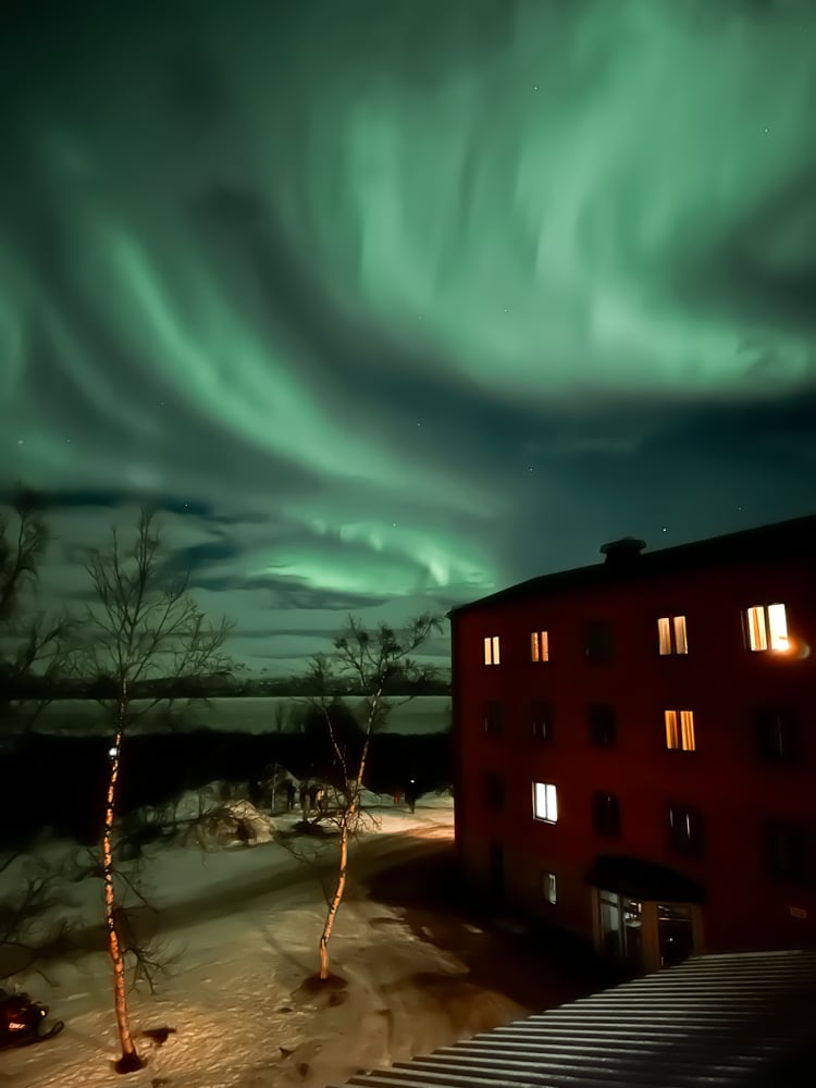 Light green northern lights swirling in the sky above Abisko tourist station hotel.