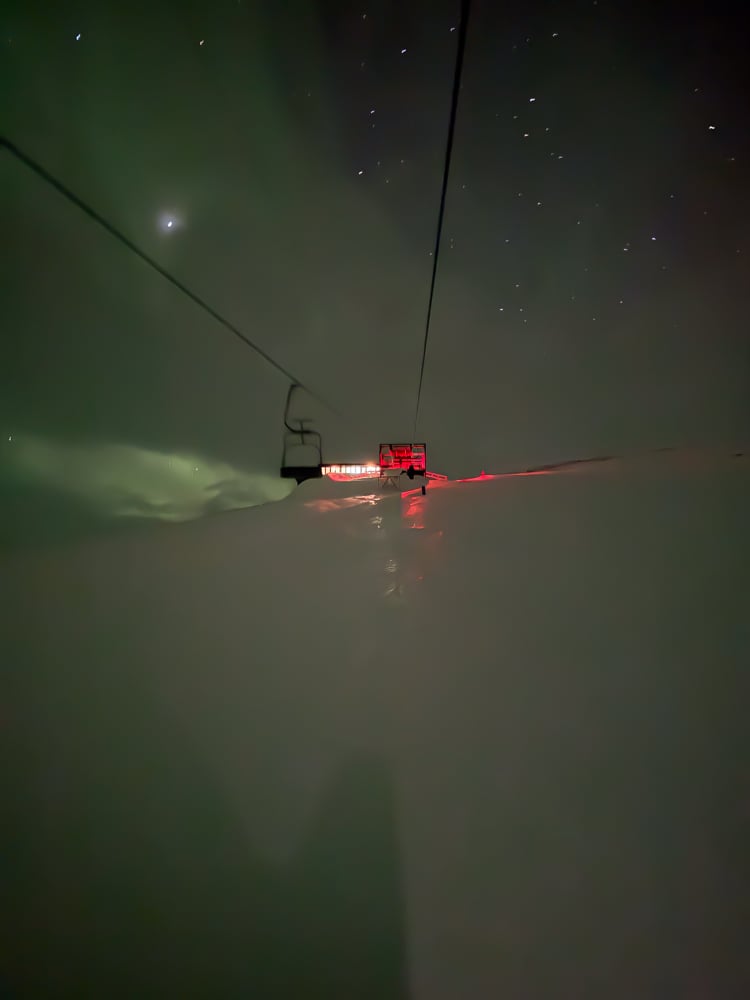 View going up the lift to the Aurora Sky Station. The ground is dark and covered in snow, and the sky kid clear and full of stars. It looks like riding a chairlift to the moon.