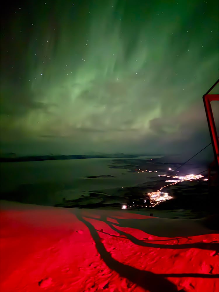 View of Abisko at night from Aurora Sky Statin. The ground is red from red lights, and the sky is full of green cloudy aurora