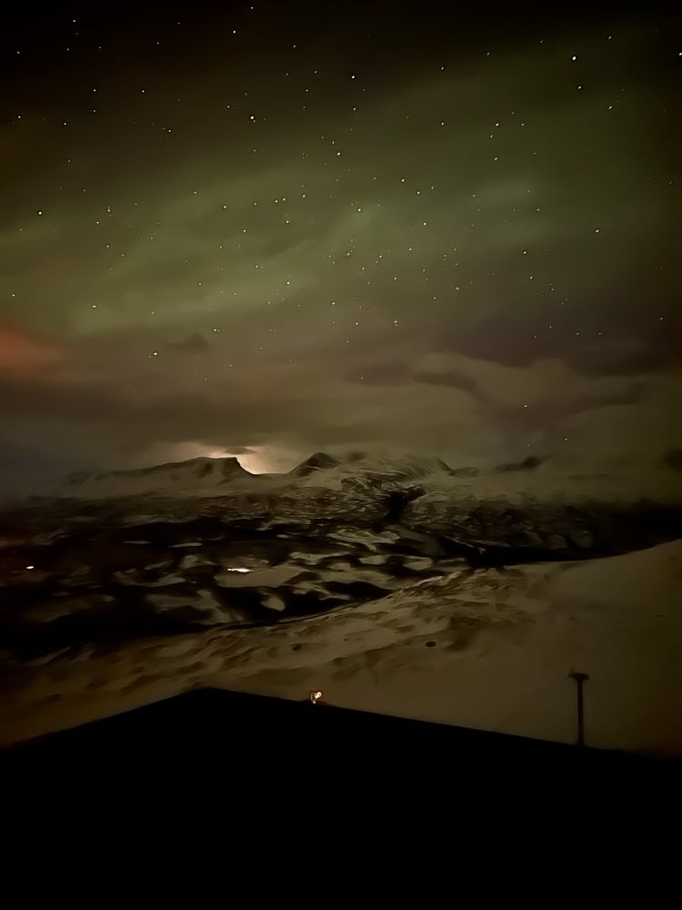 darker mountain photo with a starry sky and more faint northern lights