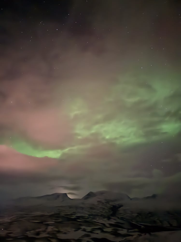 View of mountain from Aurora Skystation. The aurora are green and there's a bit of pink in the clouds.