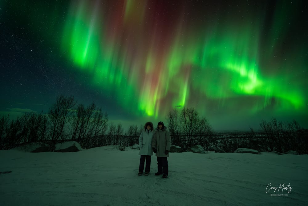 Rachelle and Pete under green and red aurora in a photograph taken by Corey Muntz.