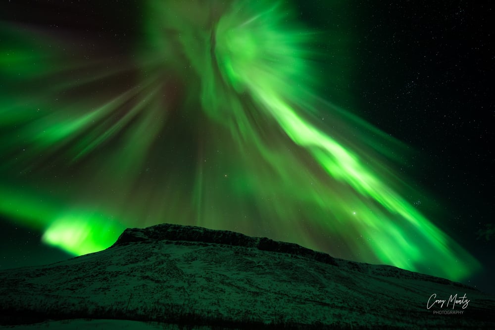 Green northern lights in the same of an angel over a mountain. Photograph by Corey Muntz