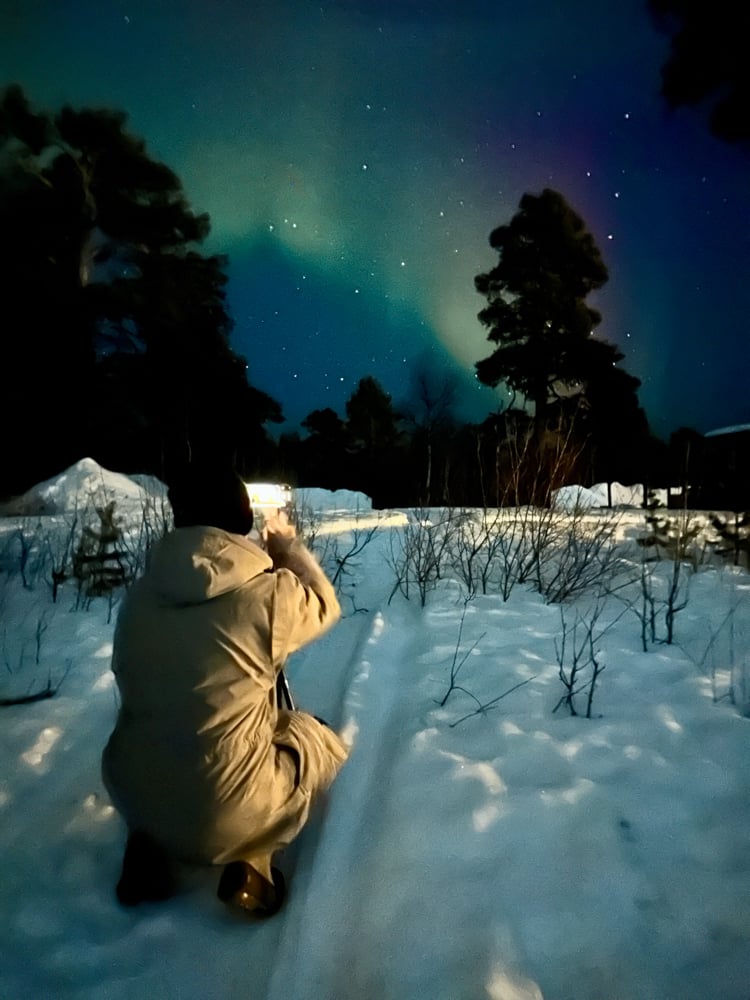 Pete squatting down in the snow to photograph the northern lights at a distance