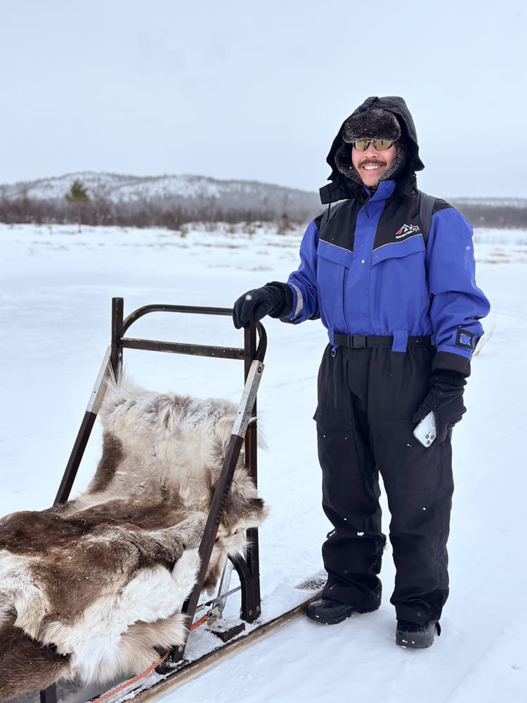 Pete dressed in a blue snowsuit standing beside a sleigh