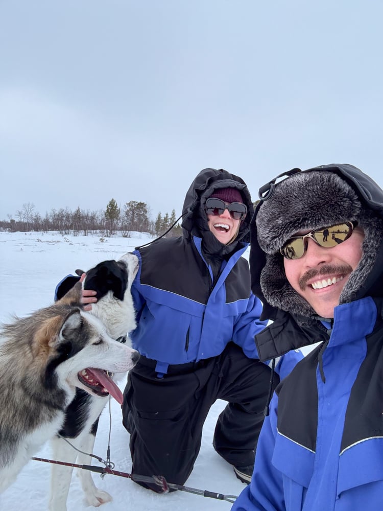 Rachelle and Pete dressed in snowsuits playing with huskys