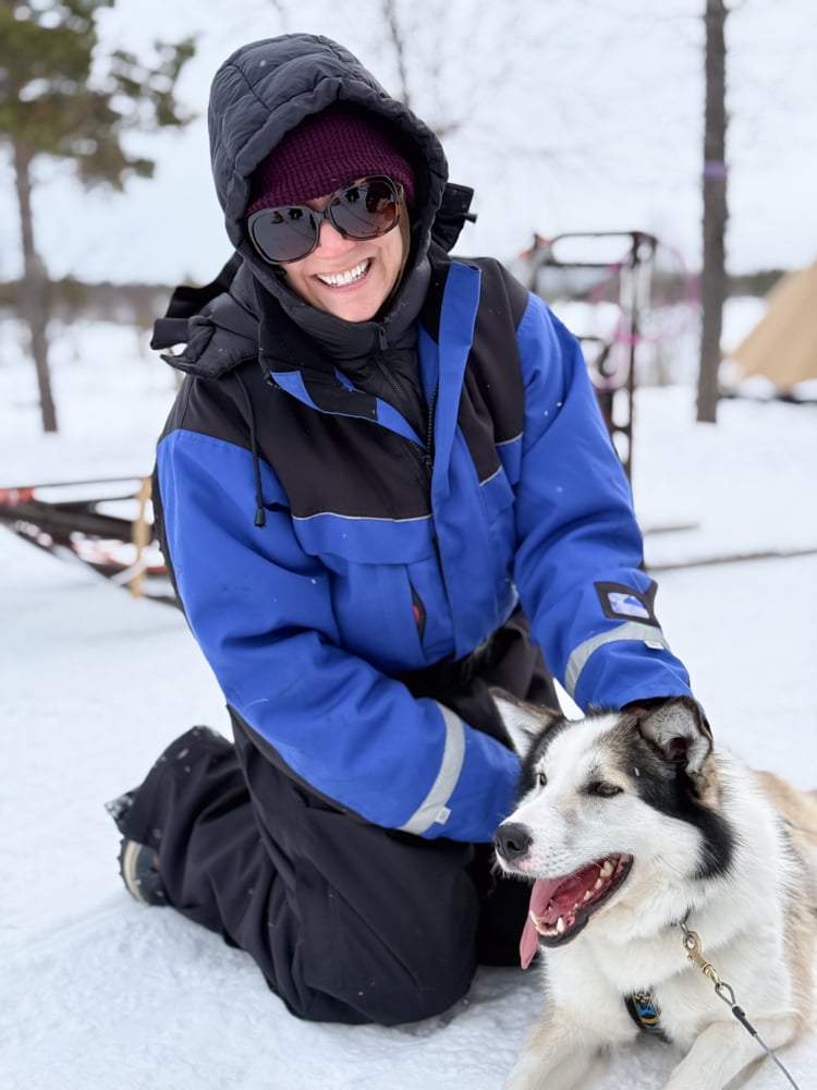 Rachelle wearing a blue snowsuit petting a husky