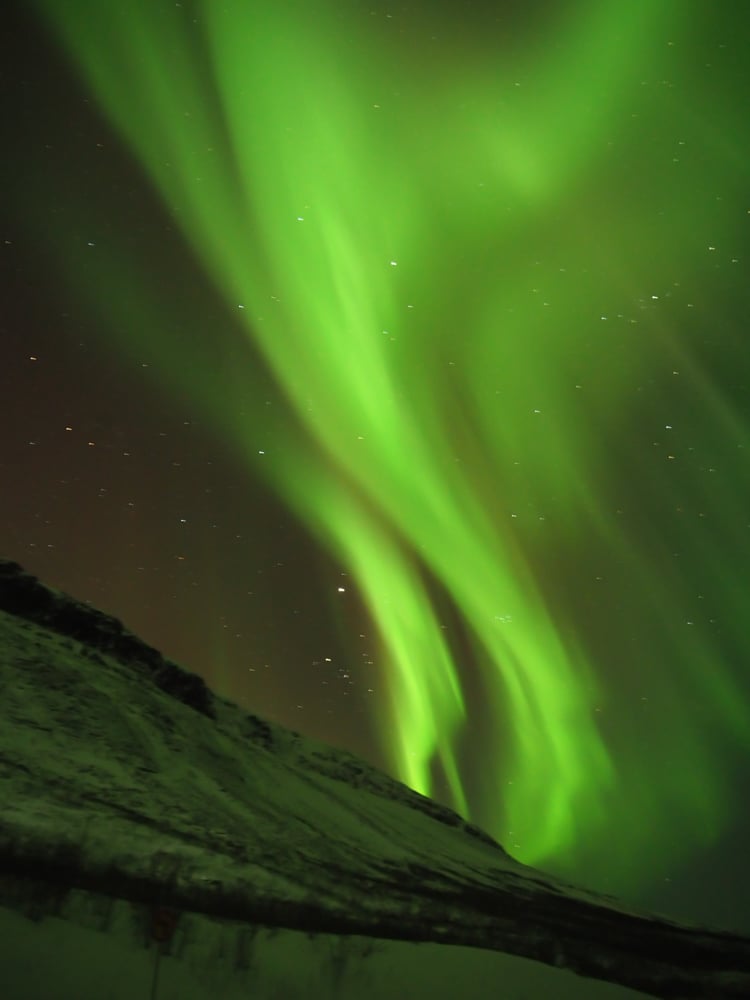 Neon green ribbons northern lights over a mountain