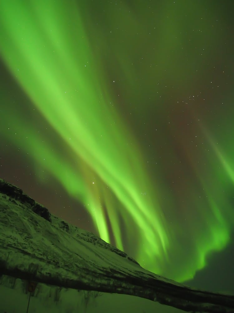 Neon green ribbons northern lights over a mountain