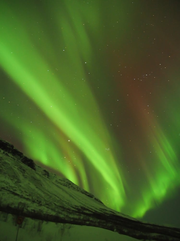 Neon green ribbons northern lights over a mountain