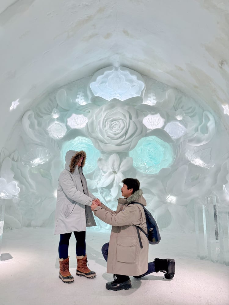 Pete on one knee holding Rachelle's hand in the ice chapel at the ice hotel