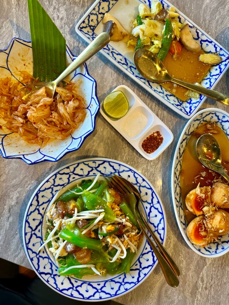 Overview of several Thai dishes, the plates are blue and white and the food is colorful.