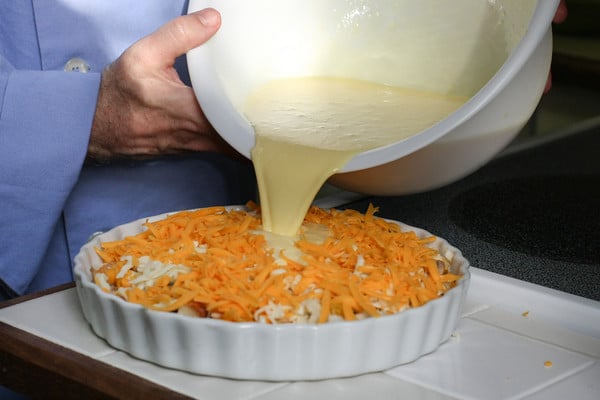 pouring egg mixture over cheese and other ingredients in breakfast strata 