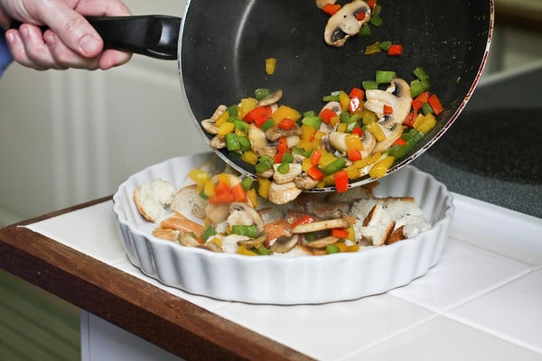 sautéed veggies being poured into pie dish 