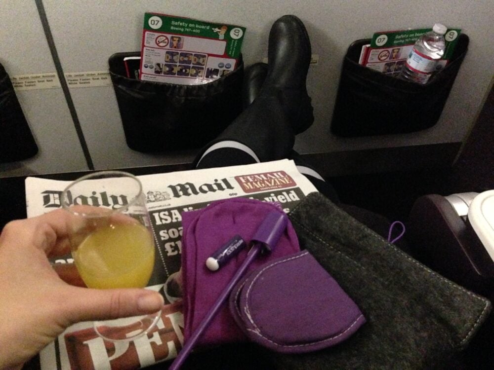 Stretching out while wearing boots and holding a glass of mimosa in Virgin Premium Economy